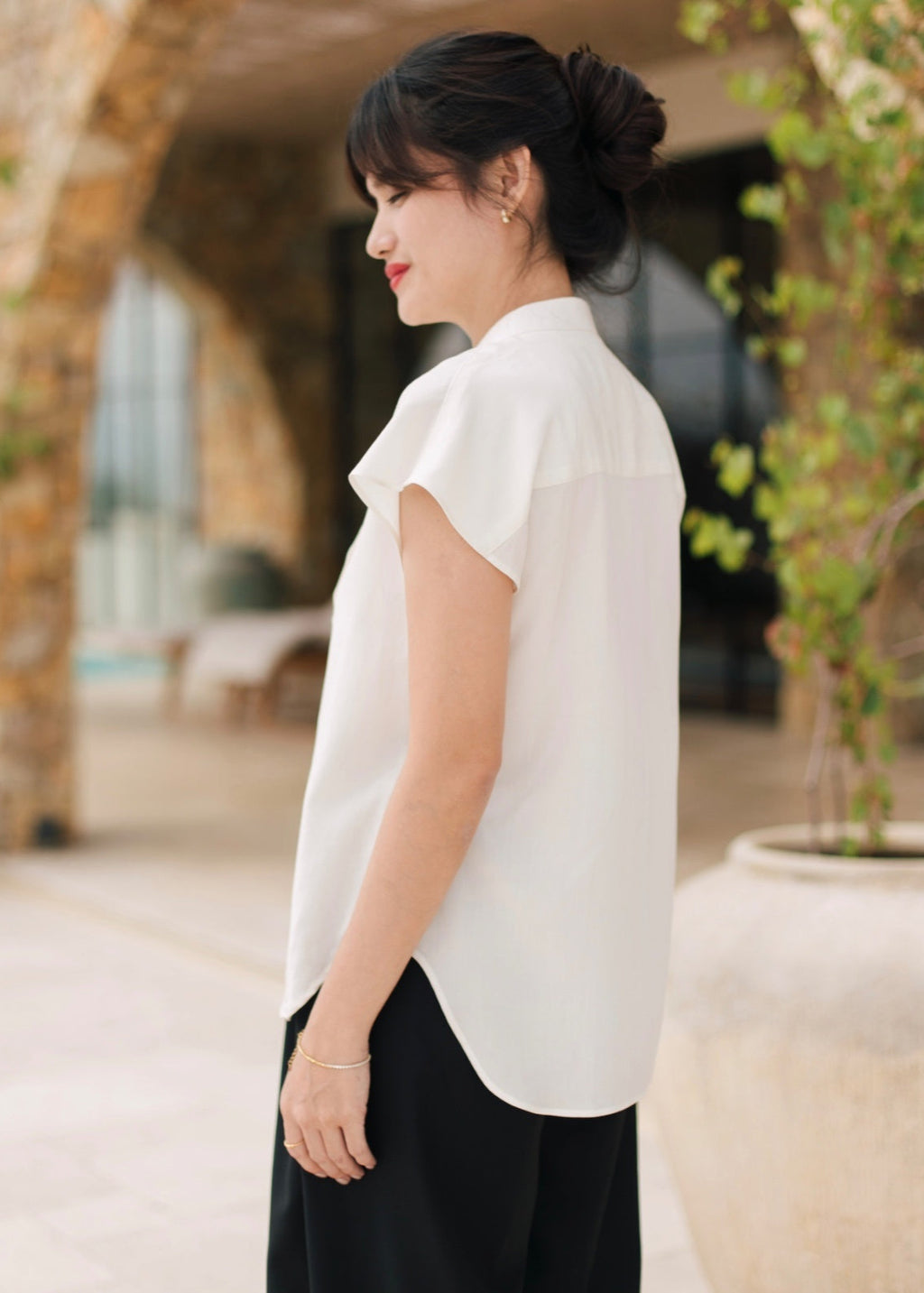 Woman wearing a white blouse and black pants standing outdoors.